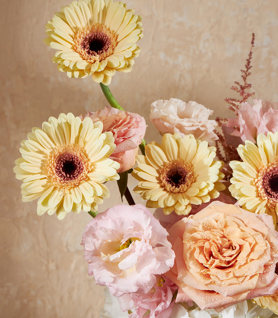 Golden yellow gerberas with pink roses and lisianthus in a fresh vase arrangement