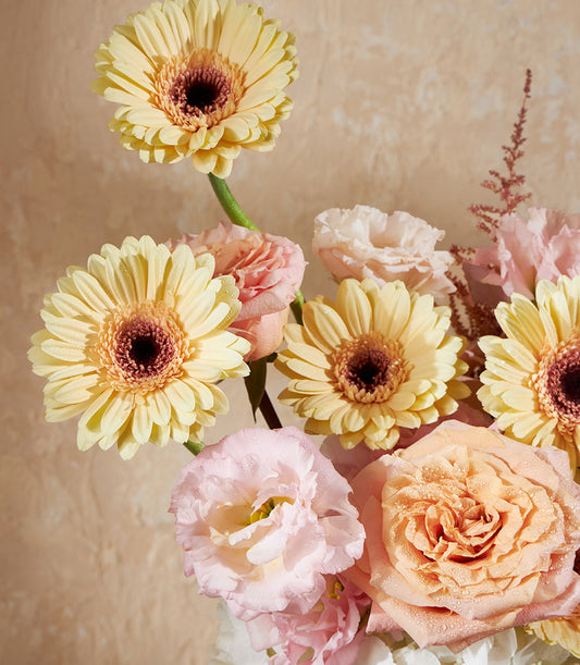 Golden yellow gerberas with pink roses and lisianthus in a fresh vase arrangement