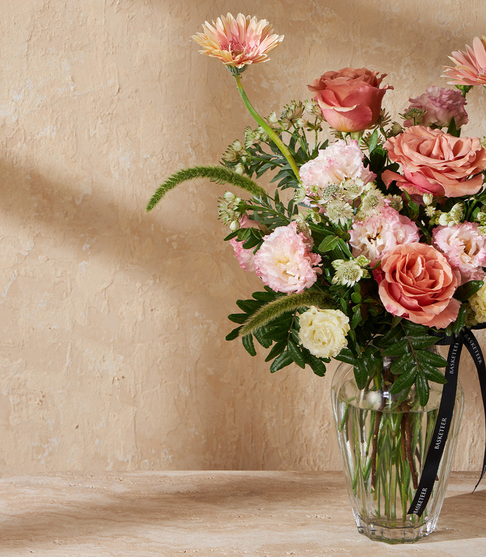 Pink and peach rose arrangement in clear glass vase with gerbera daisies and white blooms