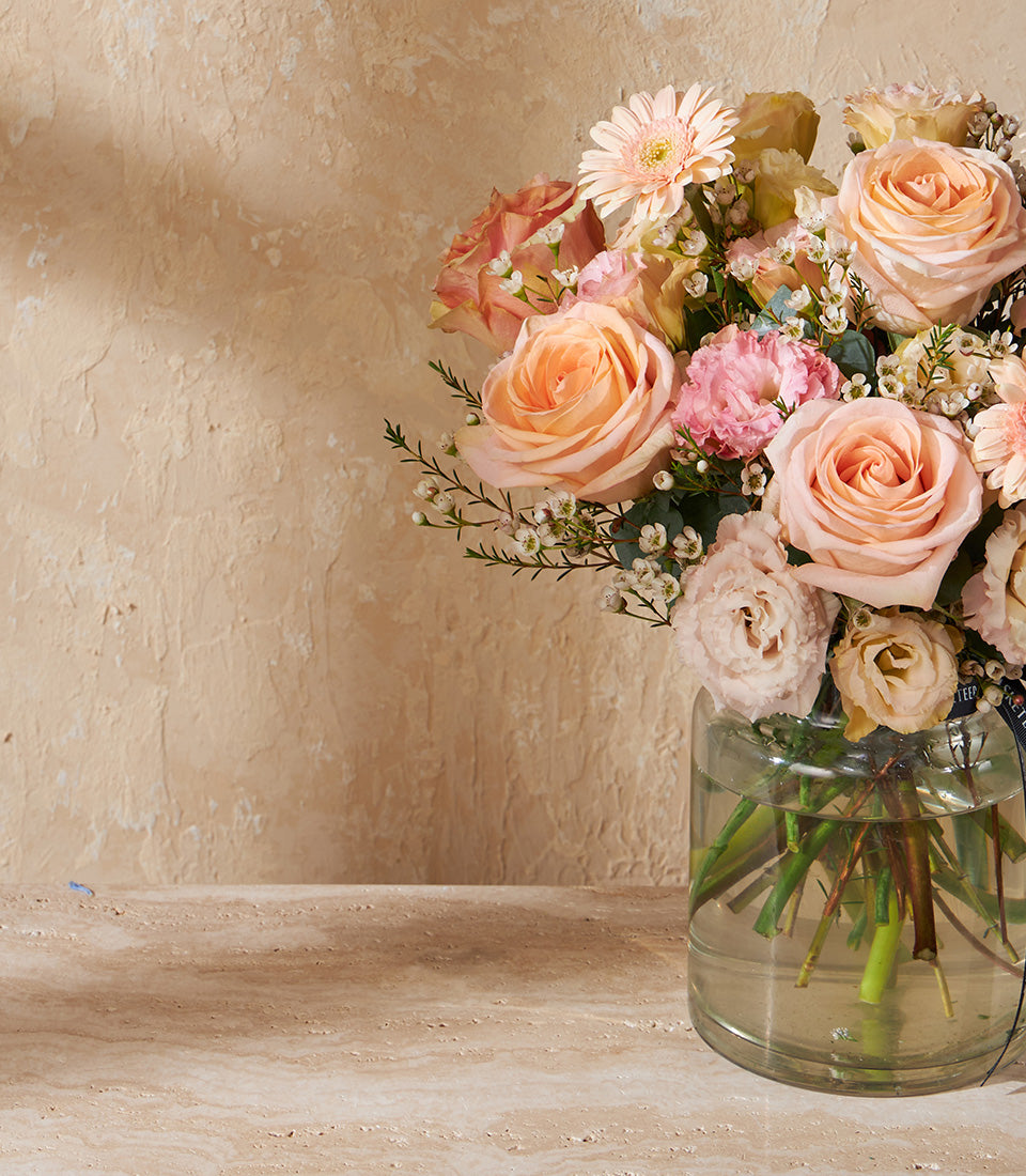 Fresh peach and pink rose bouquet in clear glass vase with gerbera daisies