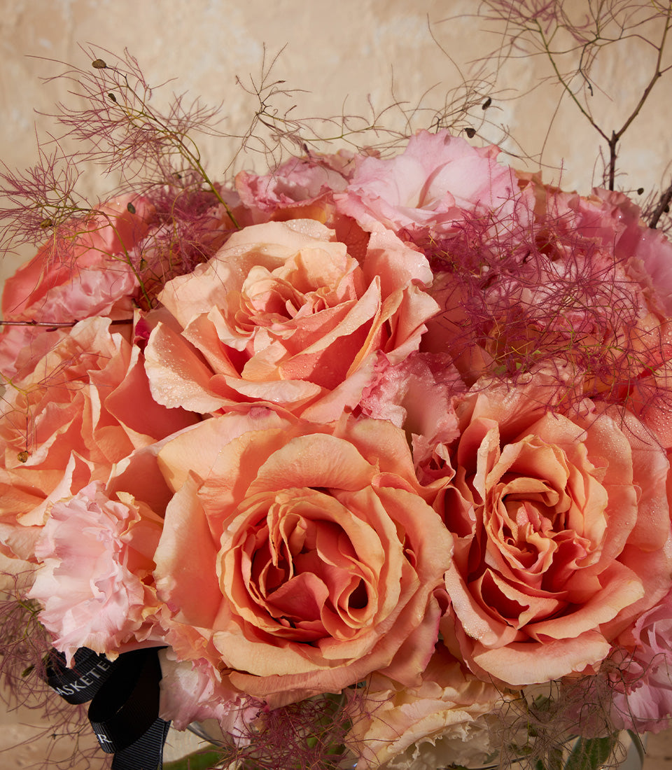 Peach and coral roses with carnations in fresh vase arrangement, tied with elegant black ribbon