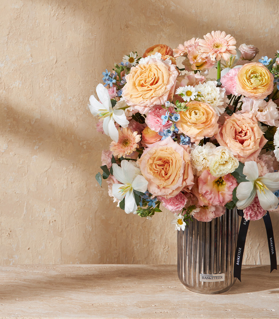 Premium peach and white floral arrangement in metallic ribbed vase with roses, lilies, and gerberas