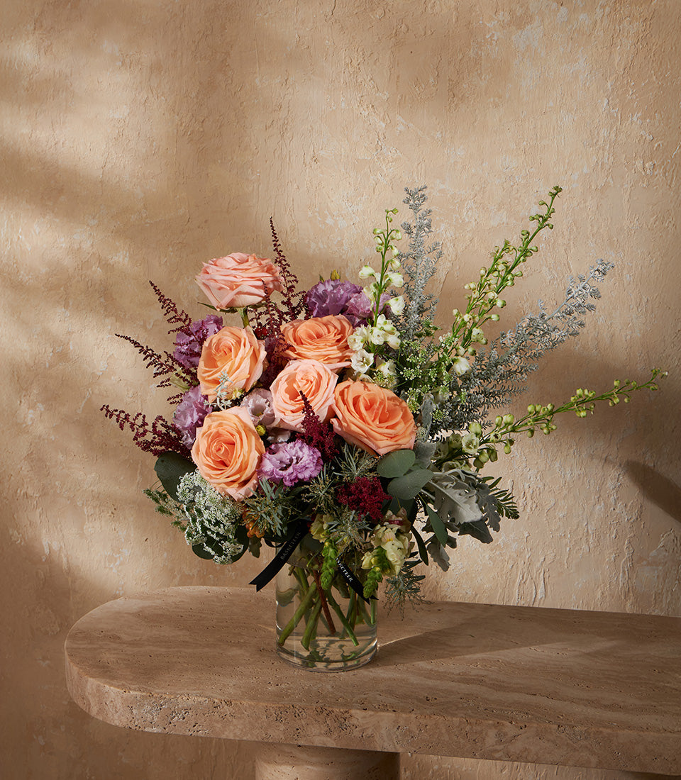 Peach roses with purple eustoma and eucalyptus in clear glass vase, artisan floral arrangement