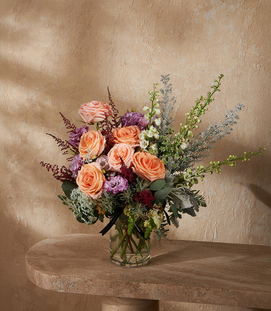 Peach roses with purple eustoma and eucalyptus in clear glass vase, artisan floral arrangement