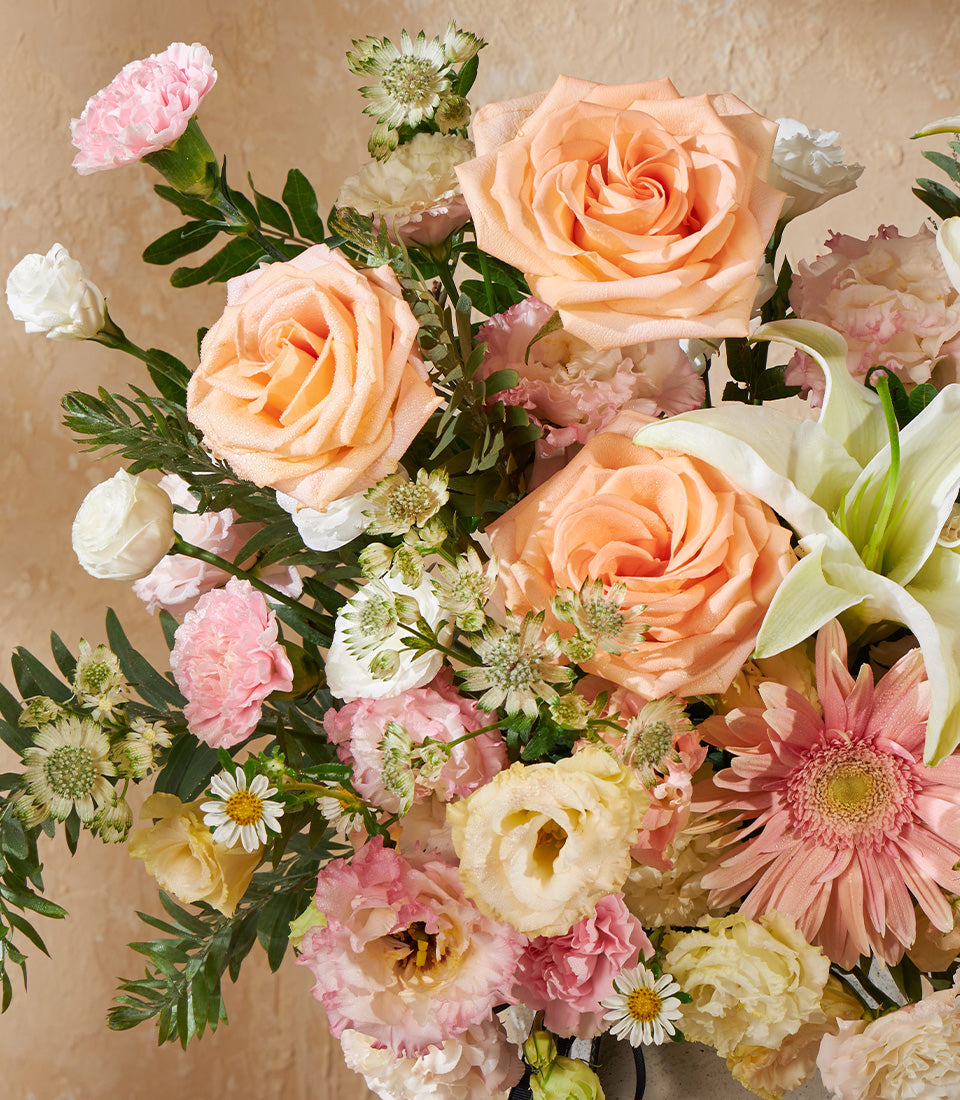 Peach roses with white lilies and pink carnations in premium vase arrangement