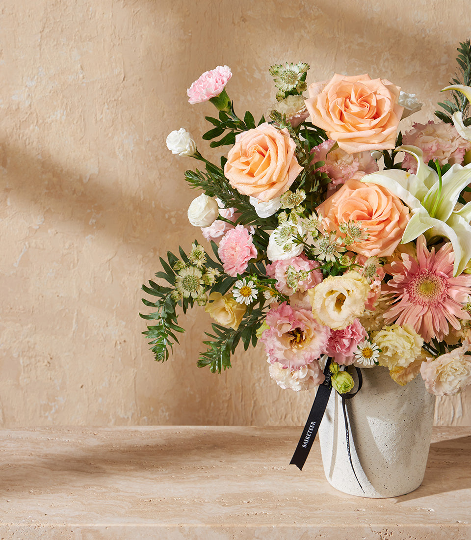 Peach roses and white lilies in textured cream vase, artisan gift arrangement