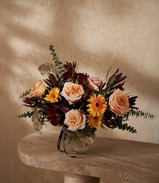 Premium peach and yellow floral arrangement in textured glass vase with burgundy foliage and eucalyptus greenery
