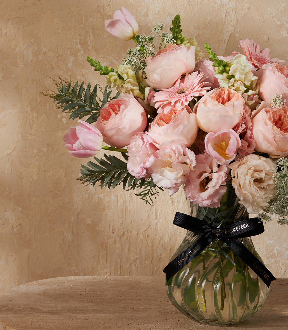 Pink roses and peonies in clear glass vase with black ribbon, luxury fresh flower arrangement