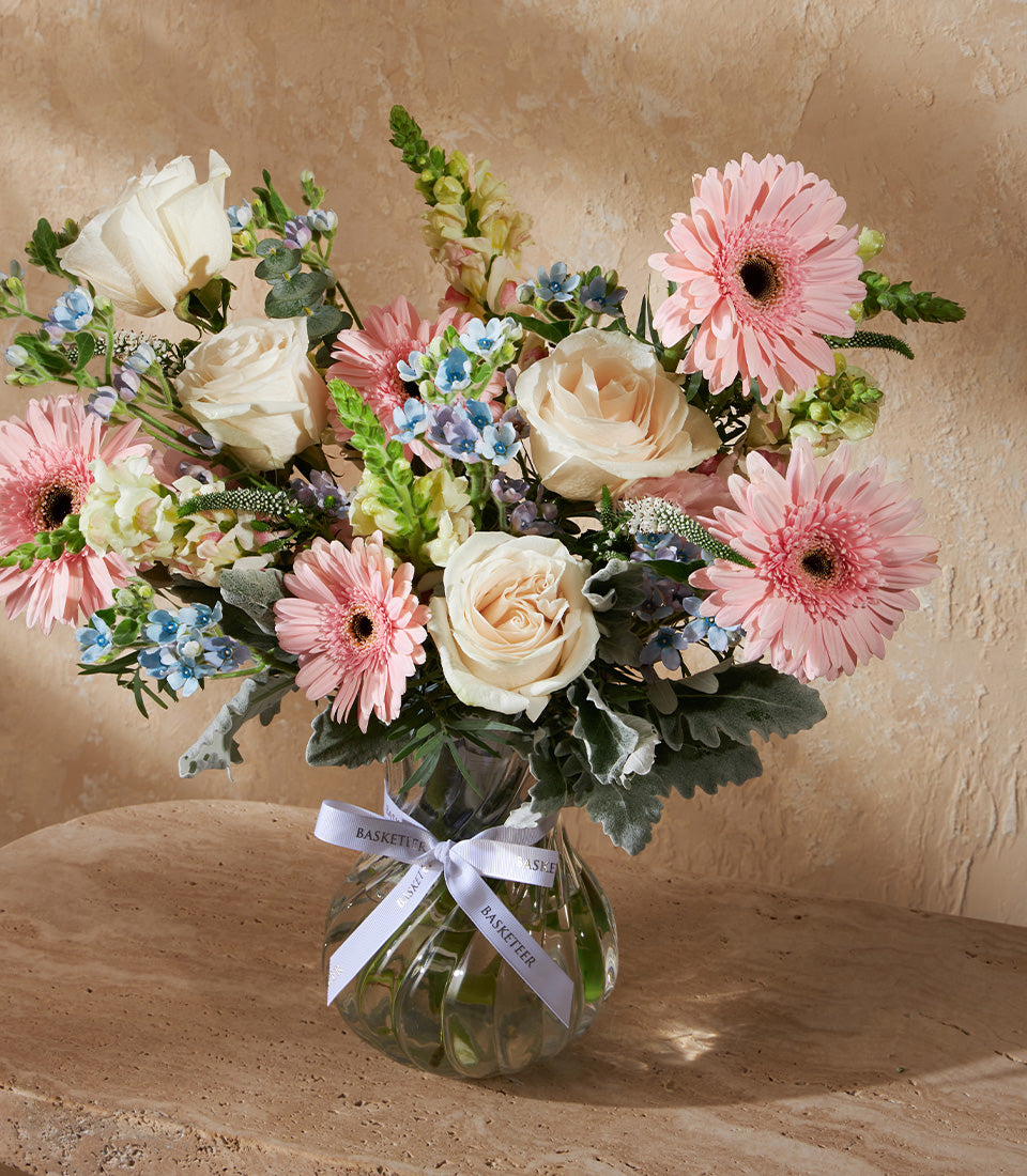 Pastel Grace vase arrangement with pink gerberas, white roses, and blue filler flowers in clear glass