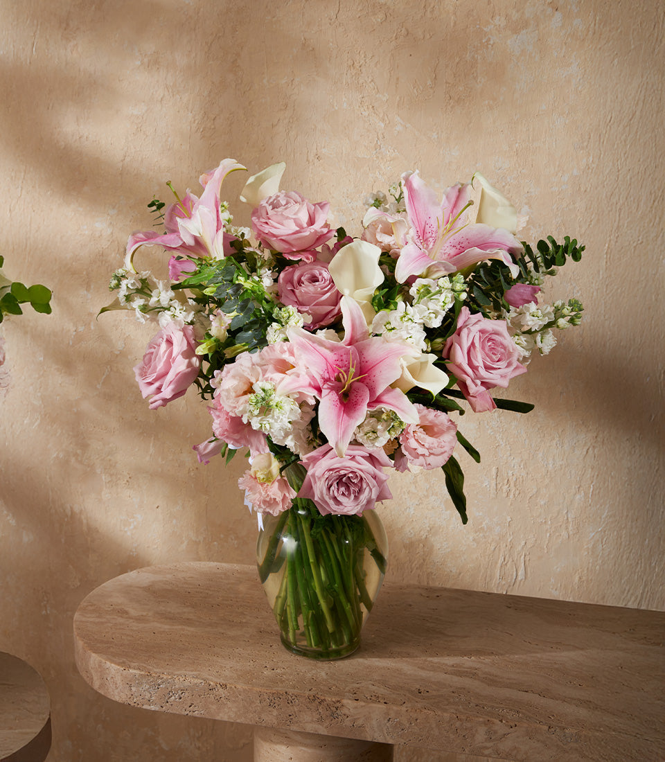 Vibrant pink roses, white calla lilies, and stargazer lilies in clear glass vase with lush greenery