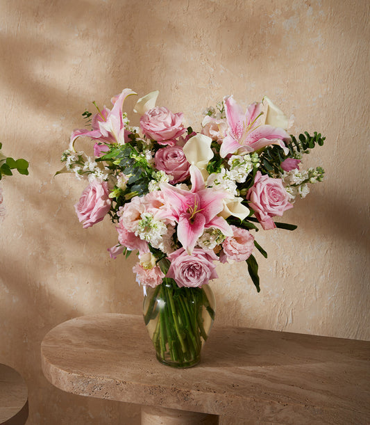 Vibrant pink roses, white calla lilies, and stargazer lilies in clear glass vase with lush greenery