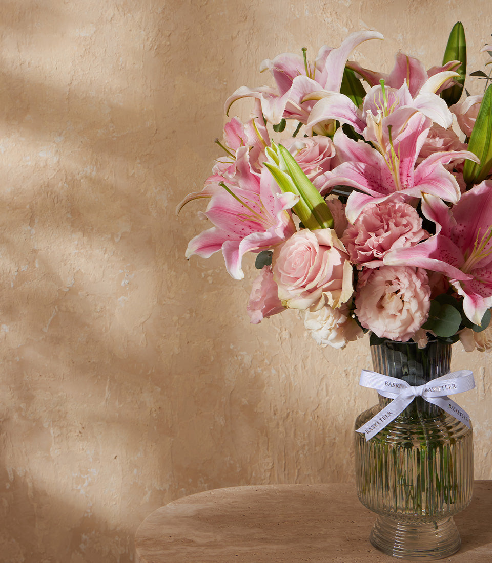 Pink lilies and roses in ribbed glass vase with white ribbon bow