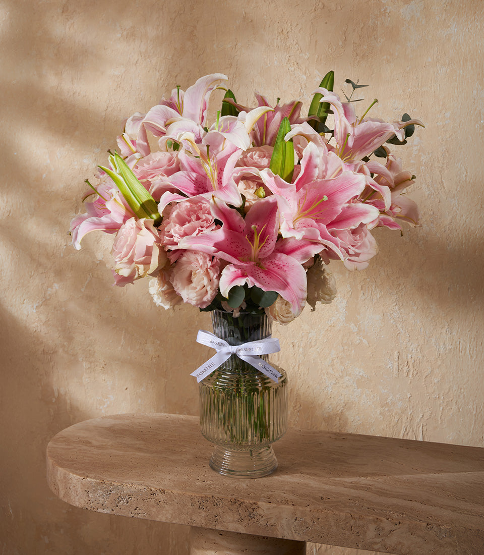 Pink and white lily bouquet with roses in clear ribbed glass vase, white ribbon
