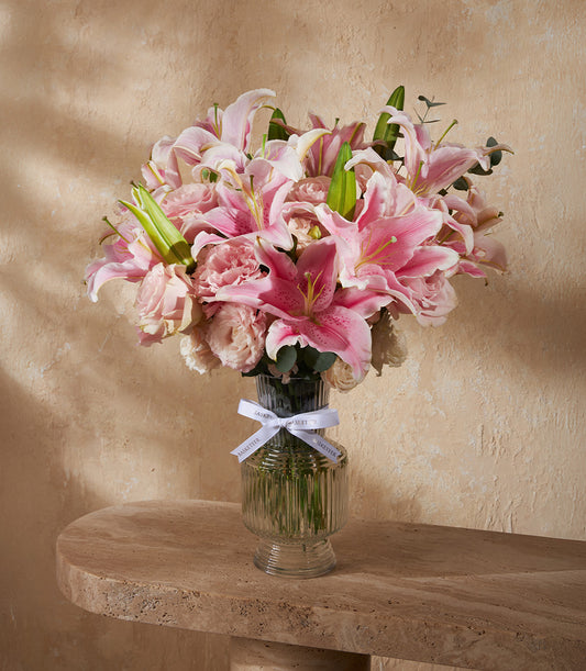 Pink and white lily bouquet with roses in clear ribbed glass vase, white ribbon
