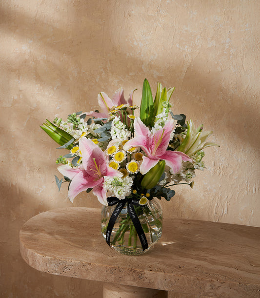 Pink lily and white flower arrangement in clear ribbed glass vase with eucalyptus and yellow accents