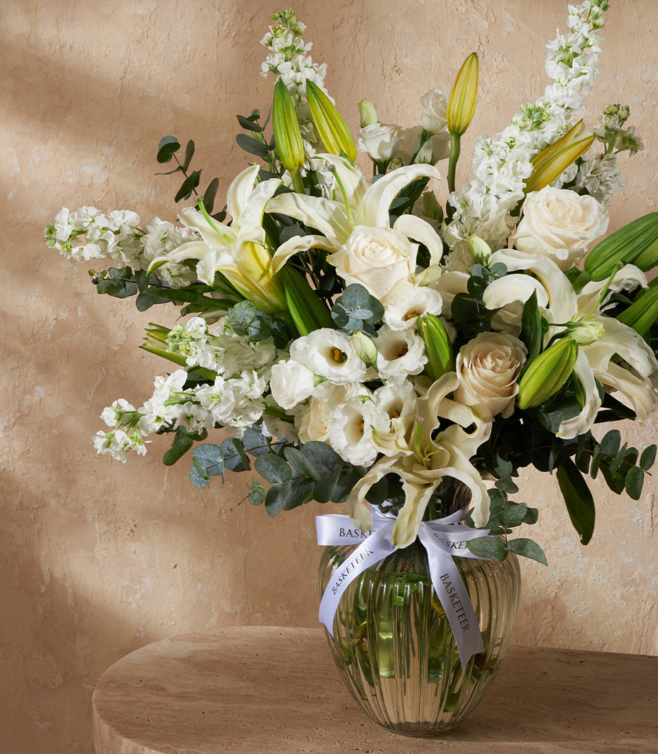 Elegant white lily and rose arrangement in ribbed glass vase with eucalyptus greenery
