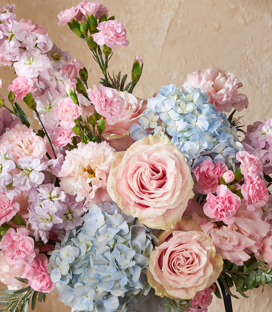 Pastel pink and blue fresh flower arrangement with roses, hydrangeas, and carnations in ceramic vase