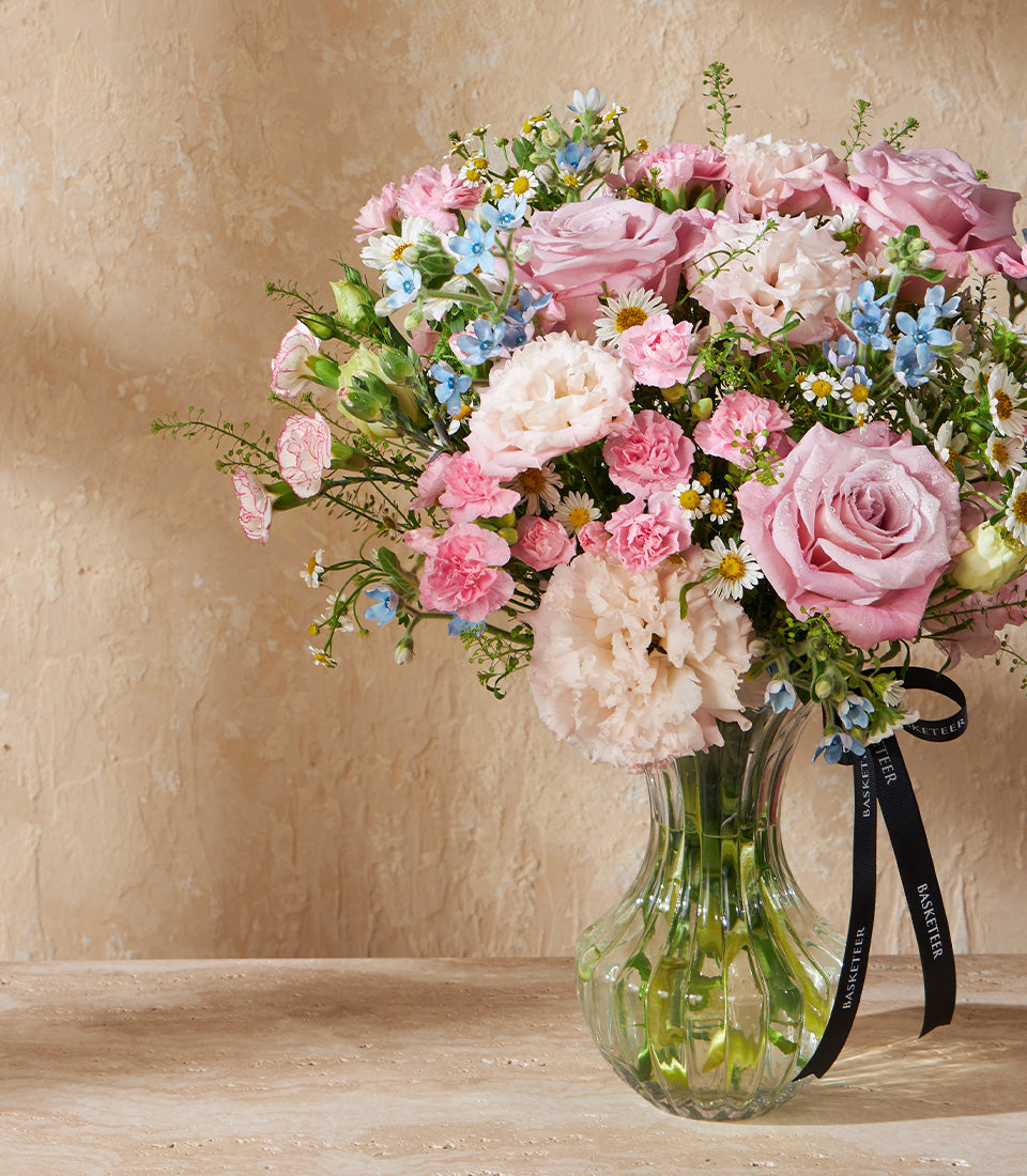 Fresh pink roses, carnations, and forget-me-nots in clear ribbed glass vase with black ribbon