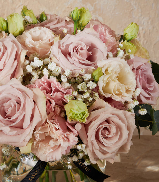 Graceful arrangement of blush roses, white lisianthus, and pink carnations in clear glass vase with eucalyptus greenery