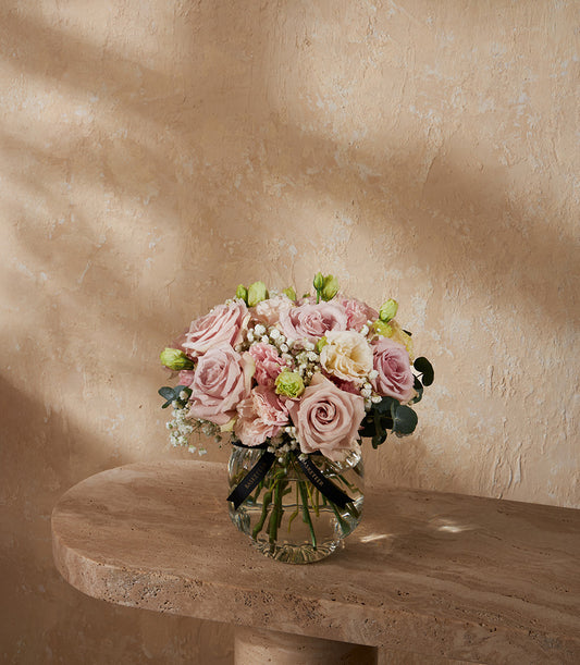 Fresh nude and cream roses with pink carnations in clear glass vase arrangement