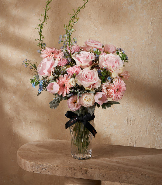 Pink rose and gerbera bouquet in fluted glass vase with blue delphinium and green foliage