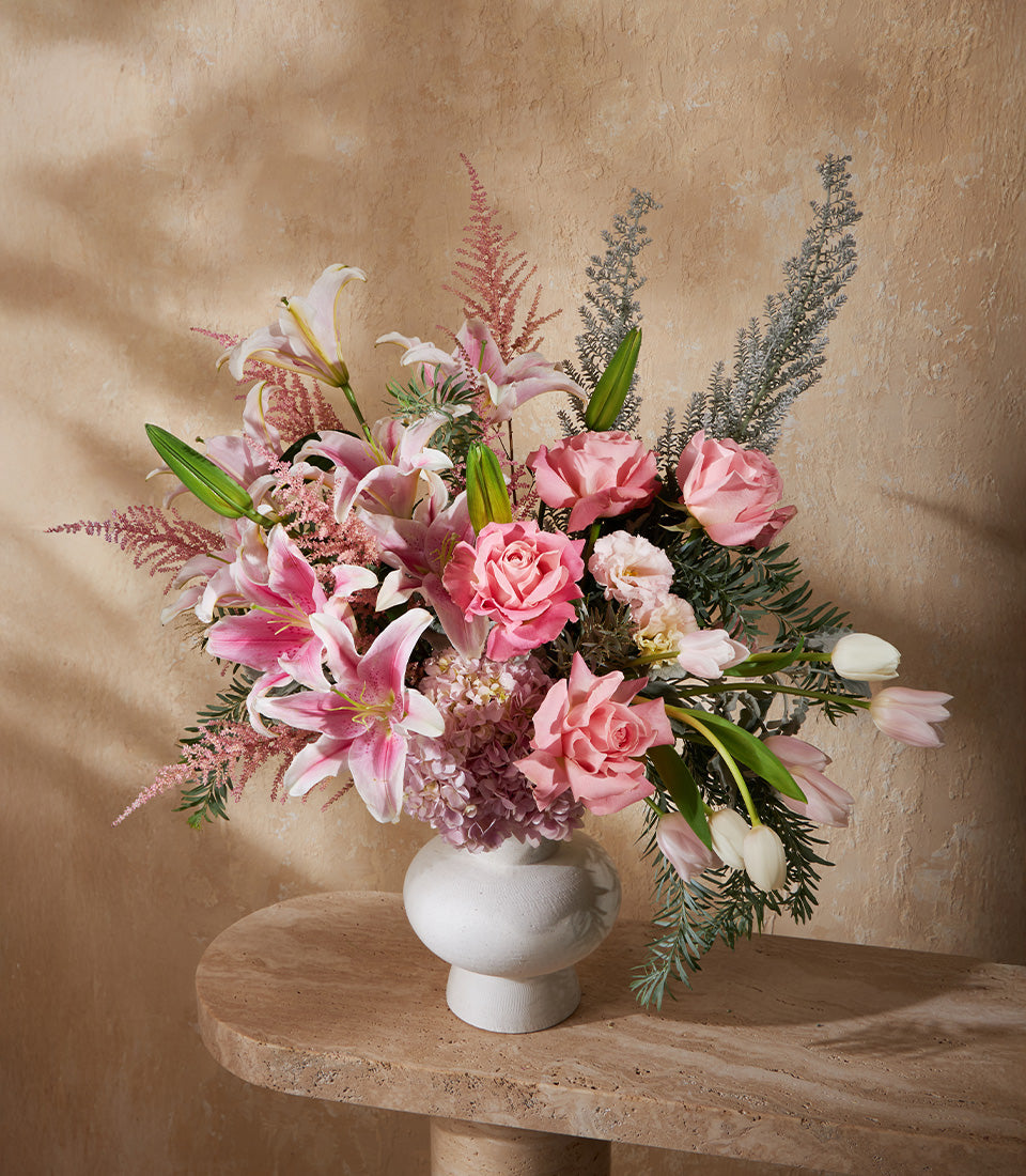 Blush pink and white floral arrangement with lilies, roses, hydrangeas in textured white ceramic vase