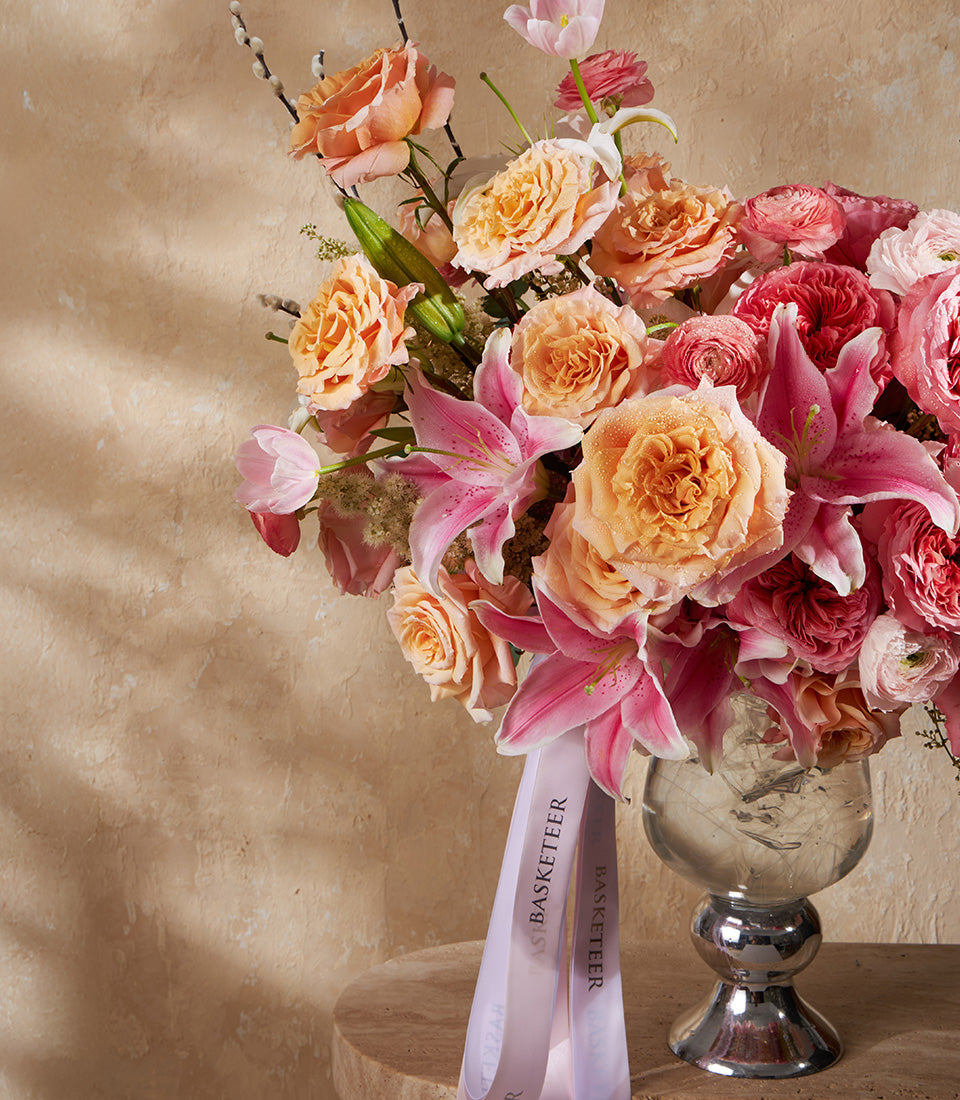 Radiant pink and peach rose arrangement with lilies and ranunculus in silver pedestal vase