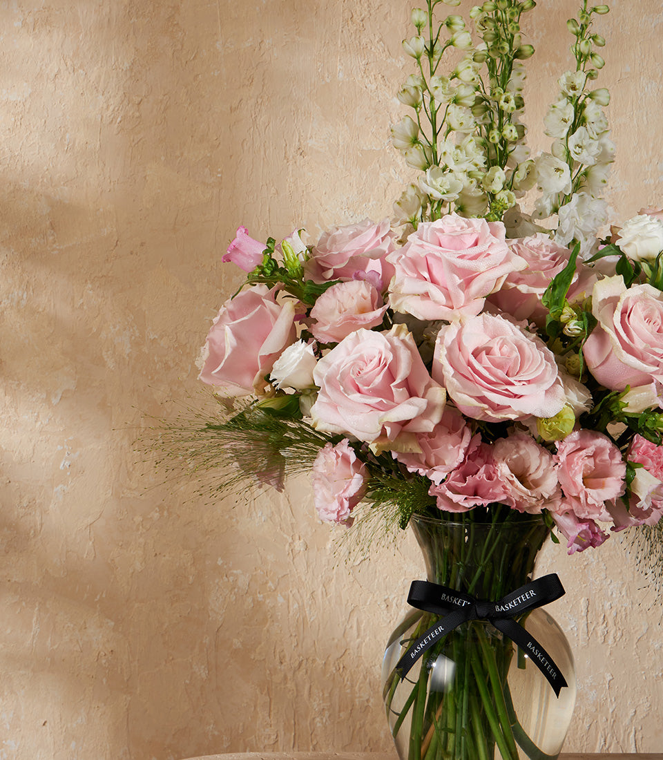 Blush pink roses and white delphiniums in clear glass vase with delicate greenery