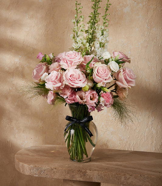 Blush pink roses with white flowers in clear glass vase, tied with black ribbon