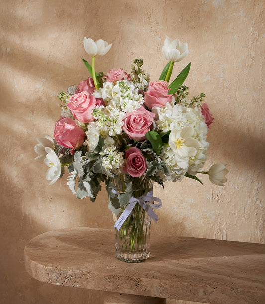 Pink roses and white tulips in elegant glass vase with grey ribbon, premium fresh flower arrangement