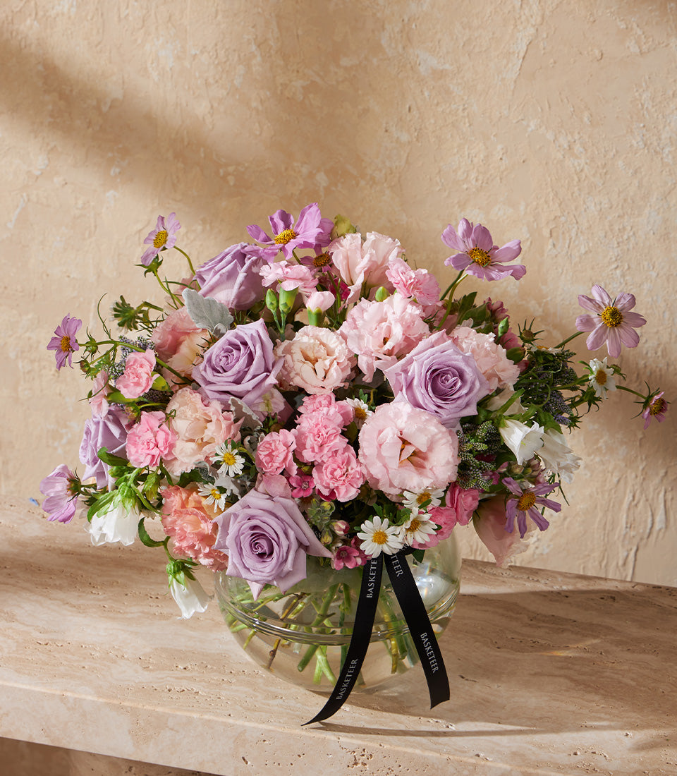 Pink and lavender roses with cosmos in spherical glass vase, tied with black ribbon
