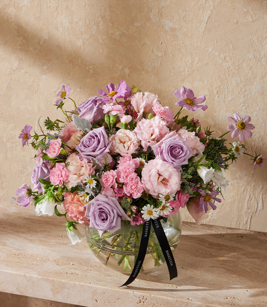 Pink and lavender roses with cosmos in spherical glass vase, tied with black ribbon