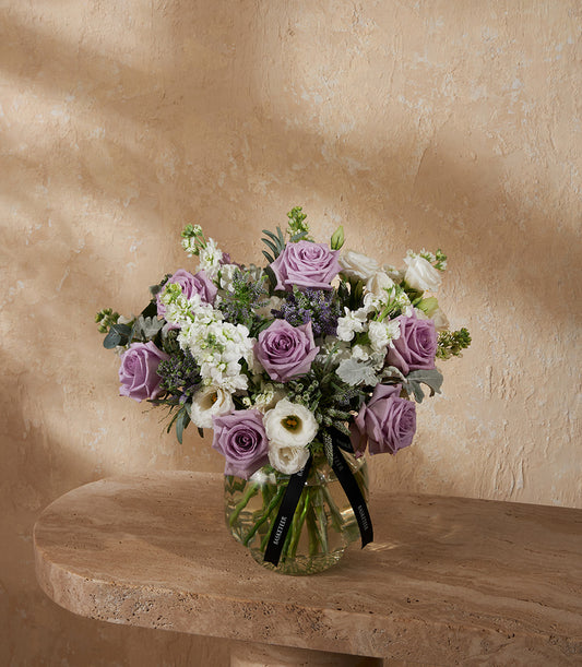 Fresh purple roses and white stock flowers in clear glass vase with silvery foliage