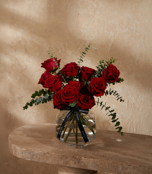Deep red roses with eucalyptus in a clear glass vase with black Basketeer ribbon
