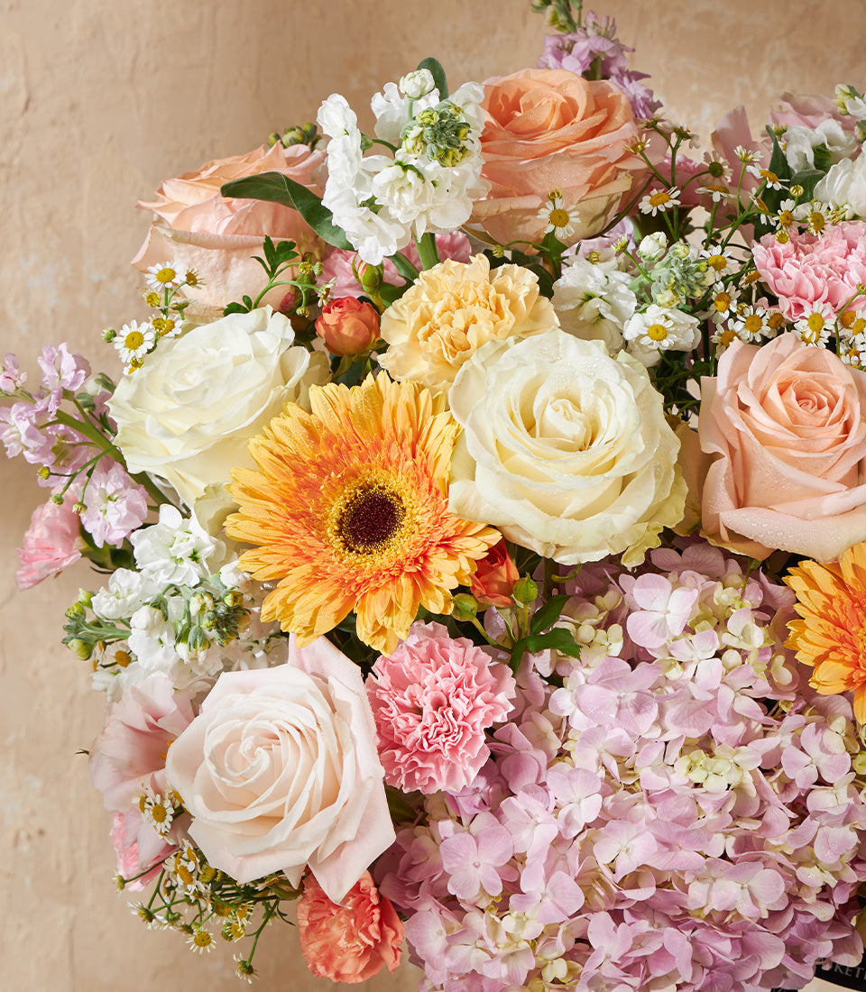 Golden dawn vase arrangement with cream roses, peach blooms, and orange gerbera in soft pastels