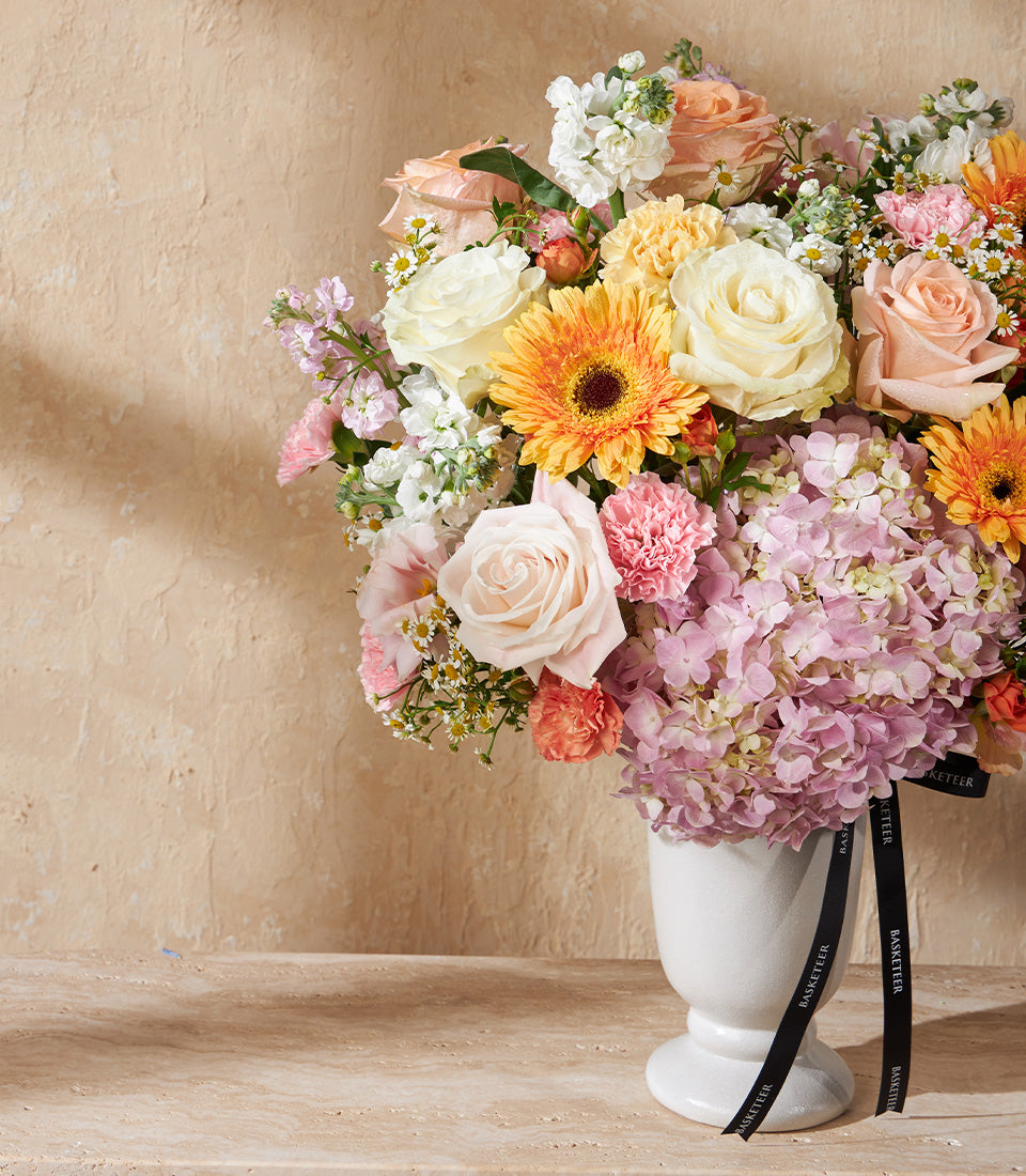 Golden Dawn floral arrangement with pink roses, orange gerberas, and hydrangeas in white ceramic vase