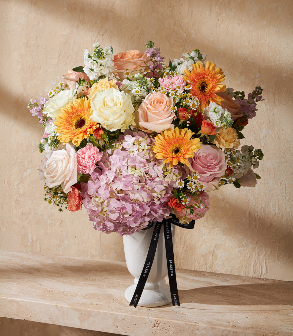 Golden Dawn premium floral arrangement with orange gerberas, pink roses, and hydrangeas in white ceramic vase