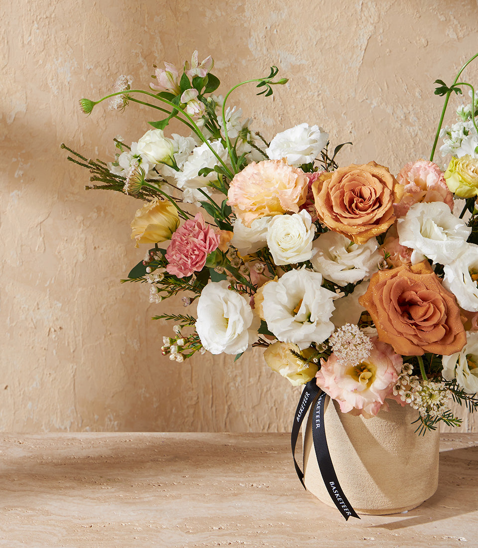 Soft peachy-pink roses and carnations in cream ceramic vase with black Basketeer ribbon
