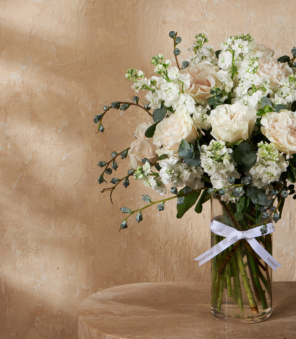 Ivory and blush roses with eucalyptus in clear glass vase, white ribbon bow