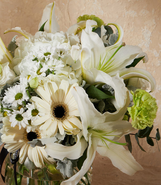 White and cream lilies, Gerbera daisies, and hydrangeas with lime green carnation in clear glass vase