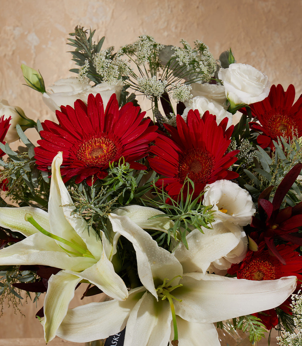 Red and white gerbera daisies with lilies and eucalyptus in a graceful mini vase arrangement