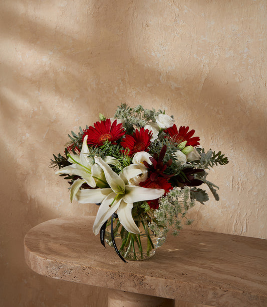 Vibrant red gerbera daisies and white lilies in clear glass vase with silk ribbon
