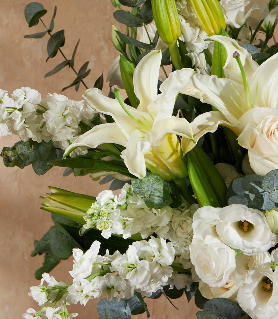 Elegant white lily vase arrangement with roses, stock flowers, and eucalyptus greenery