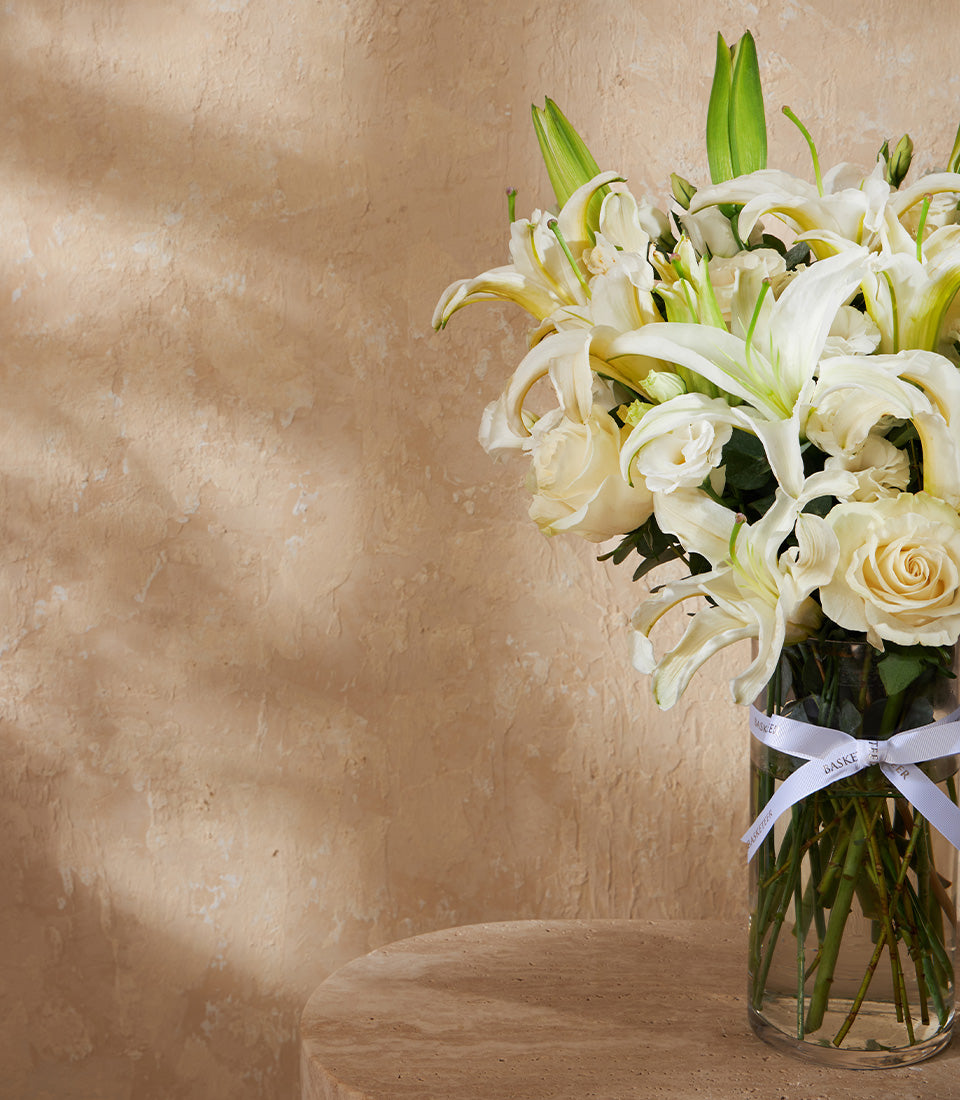 White lilies and roses in clear glass vase with silk ribbon, elegant floral gift arrangement