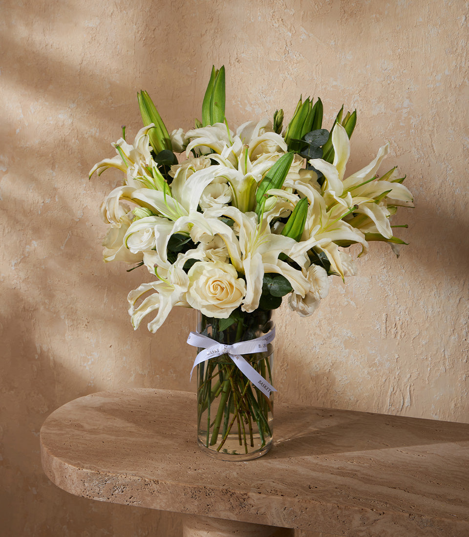 White lilies and roses in clear glass vase with white ribbon, fresh flower gift arrangement