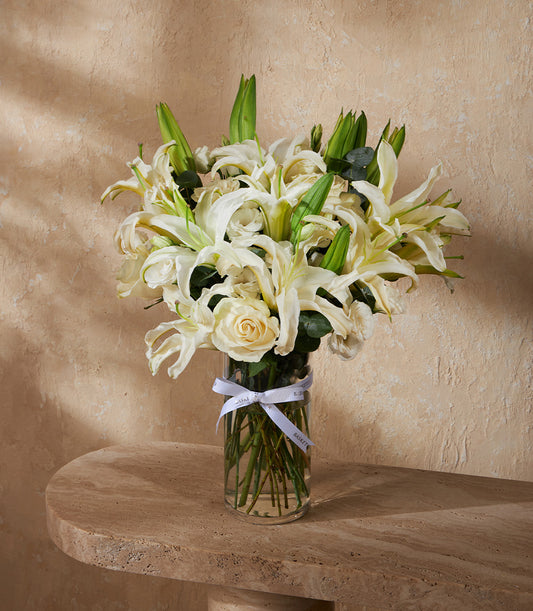 White lilies and roses in clear glass vase with white ribbon, fresh flower gift arrangement