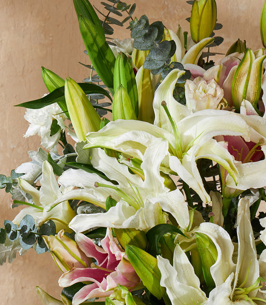 Fresh white and pink lily vase arrangement with eucalyptus and green foliage, soft neutral backdrop