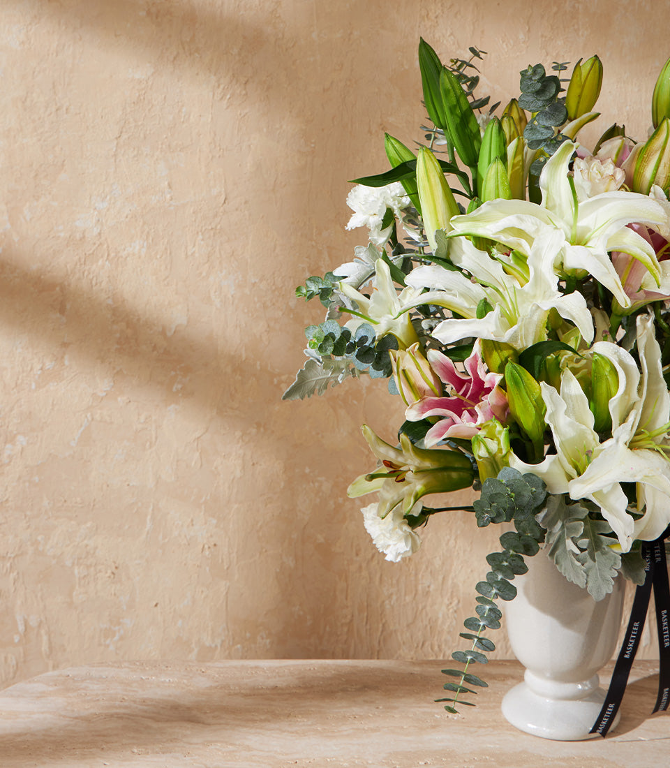Elegant white lily arrangement with pink accents and eucalyptus in fluted ceramic vase