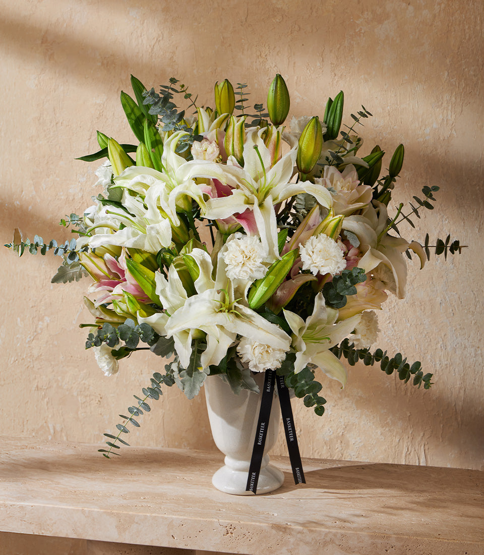 Elegant white lily and carnation arrangement in fluted ceramic vase with eucalyptus greenery