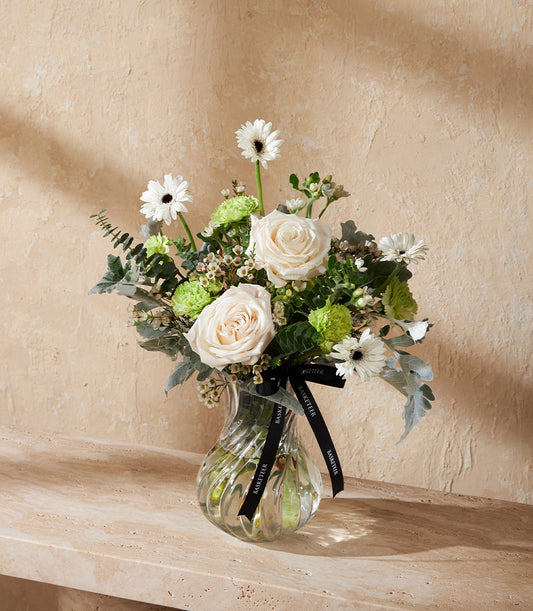 Elegant ivory roses and white gerberas with green carnations in ribbed glass vase